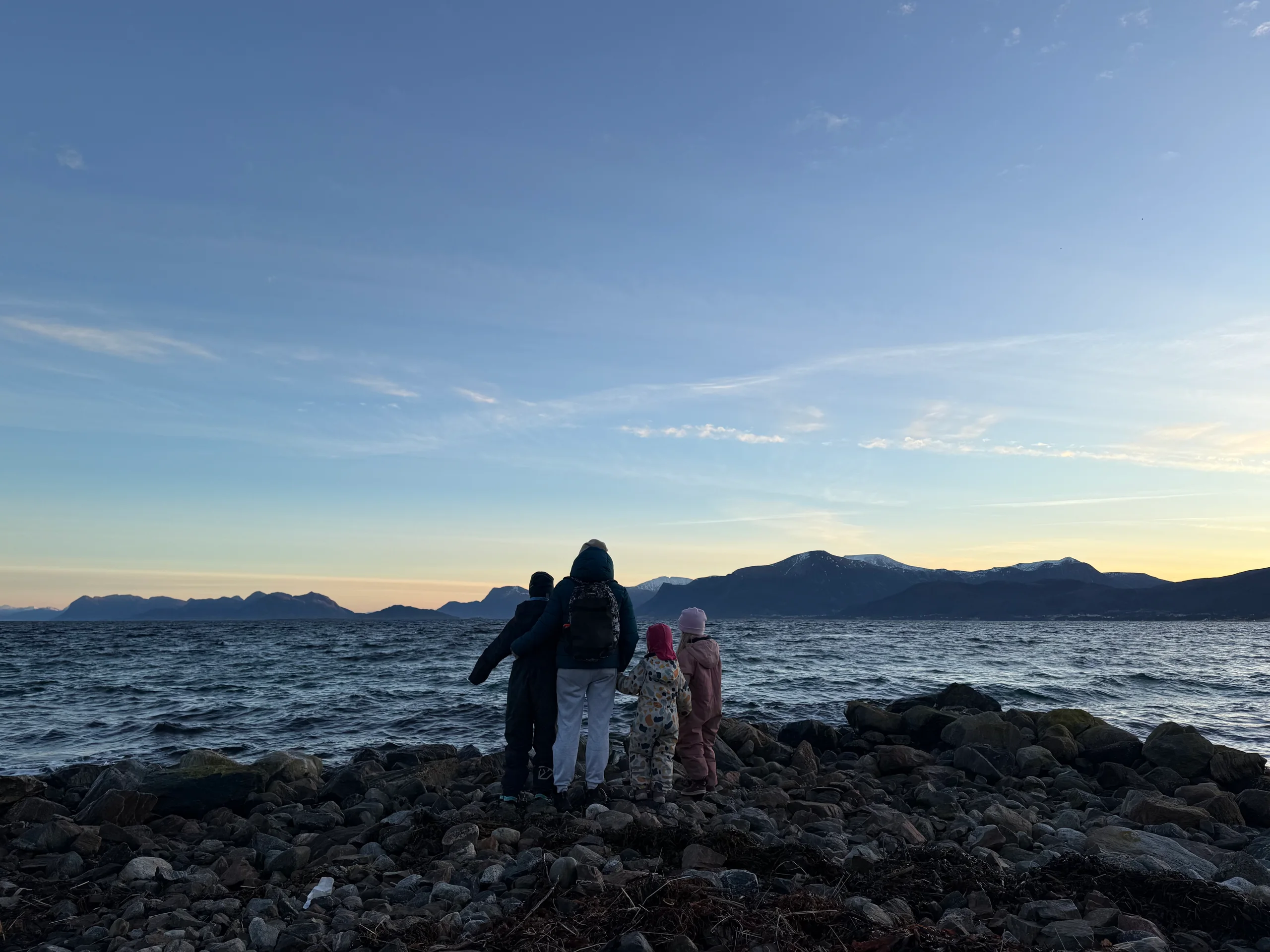 Ein familie ser utover sjøen frå fjæra på Nordøyane